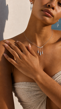 Woman wearing a silver necklace and earrings against a neutral background